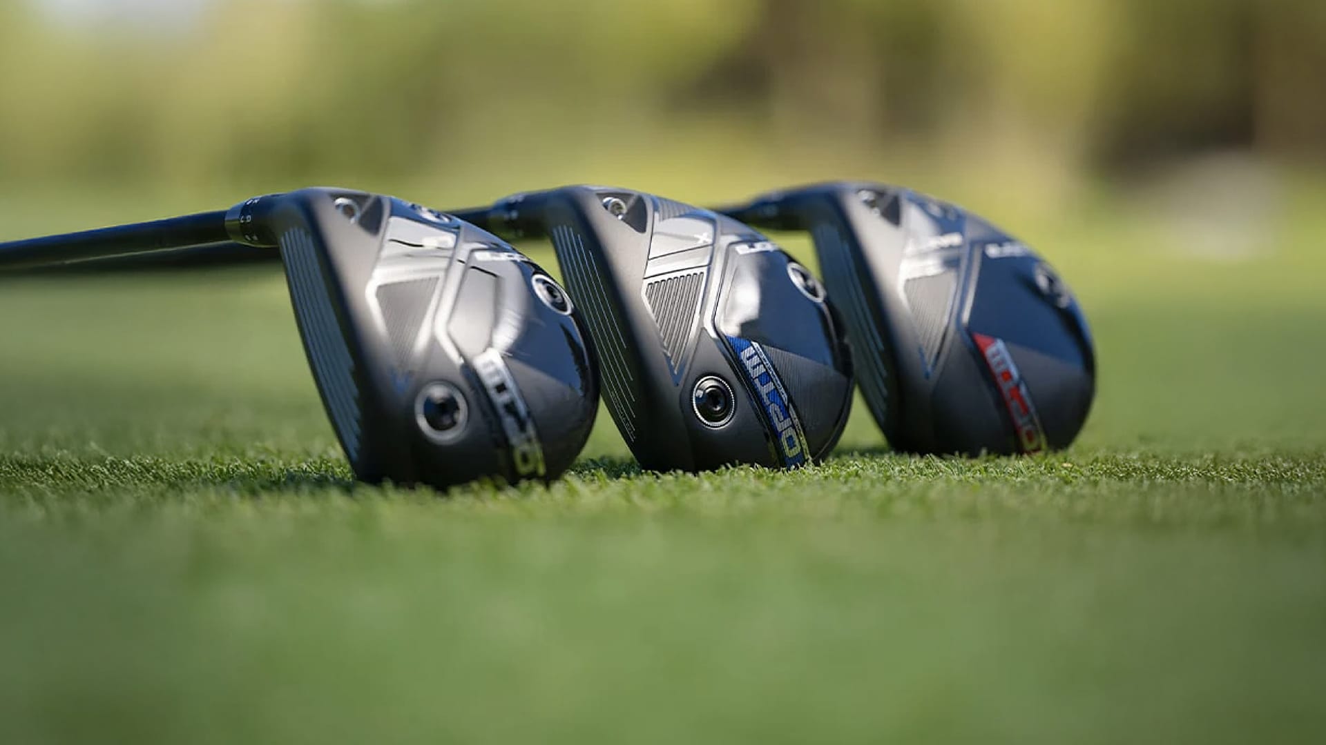 Three golf club heads on a grassy surface with a blurred background